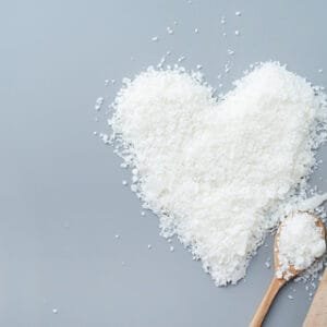 white Phytomulse Coconut Emulsifier flakes in shape of a heart in wooden spoon on blue background