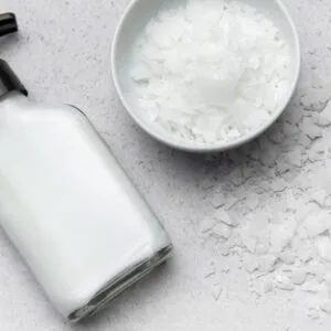 Glyceryl Monostearate (GMS) white flakes in white bowl with a lotion bottle on white background